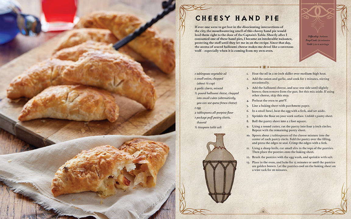 An open cookbook page shows the 'Cheesy Hand Pie' recipe on the right, with golden-brown hand pies, one broken open, on a wooden board to the left