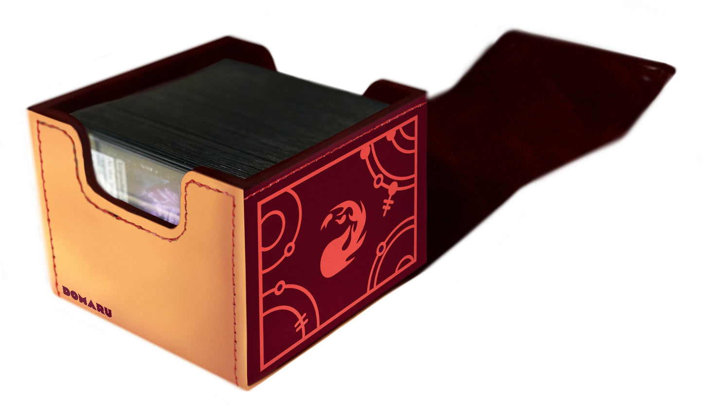 A two-tone Domaru leather deck box holding trading cards, featuring tan sides and a maroon front panel with an abstract coral-red phoenix design