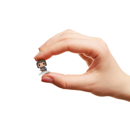 Hand holding a tiny, stylized collectible miniature figure between the thumb and index finger