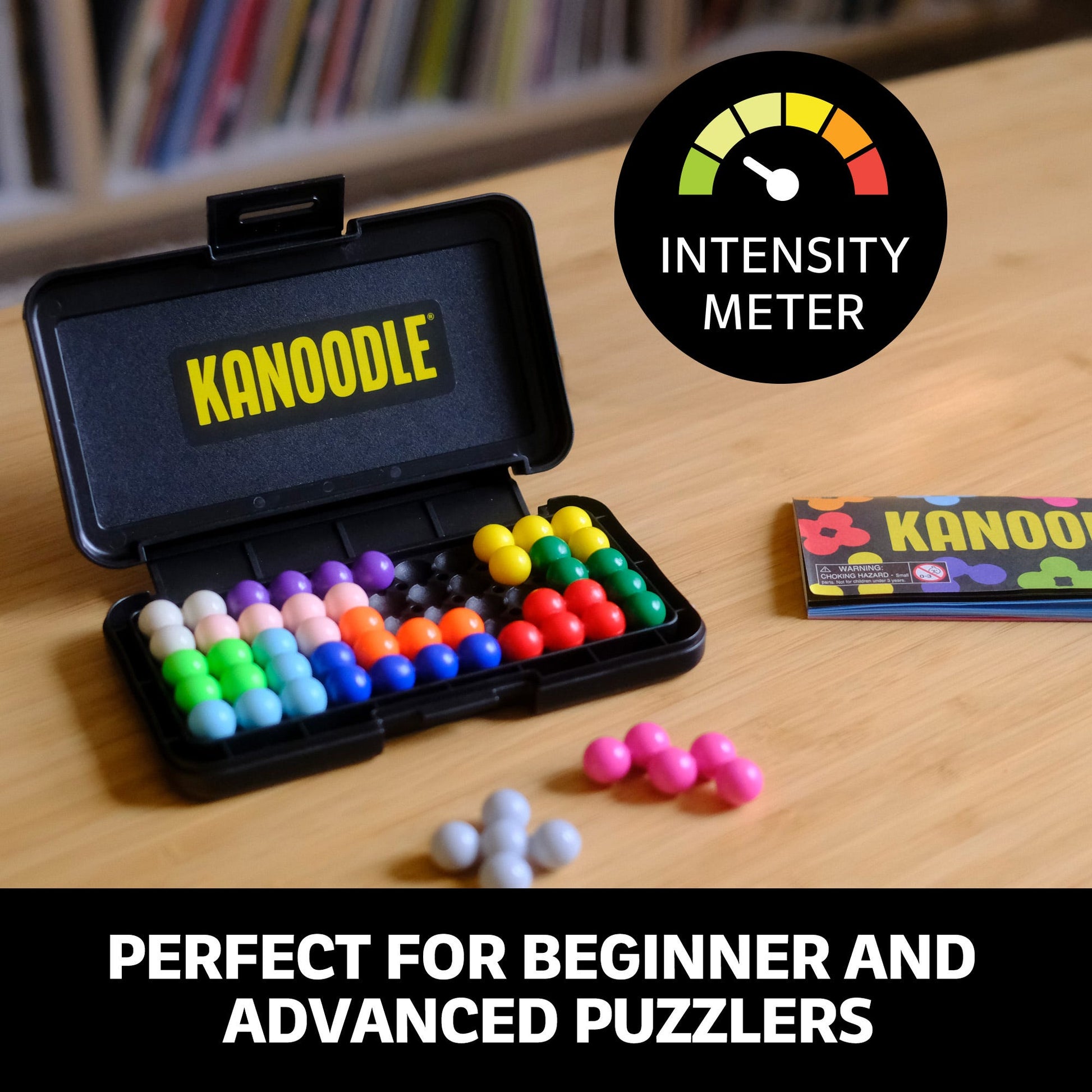 Open Kanoodle puzzle case showing colourful, interlocking spherical pieces and the instructions booklet on a wooden table