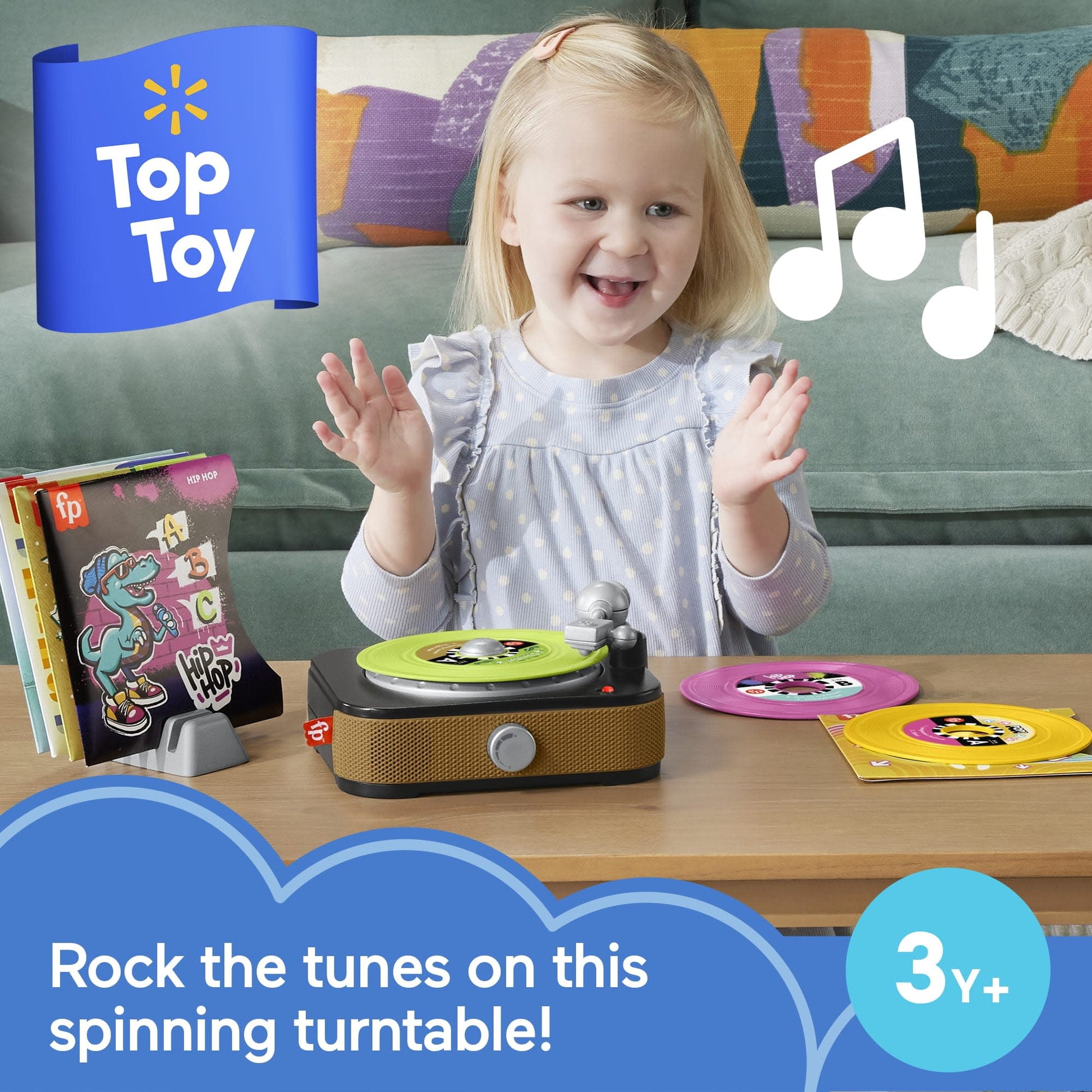 Smiling toddler claps while looking at a toy turntable with a green record and musical notes