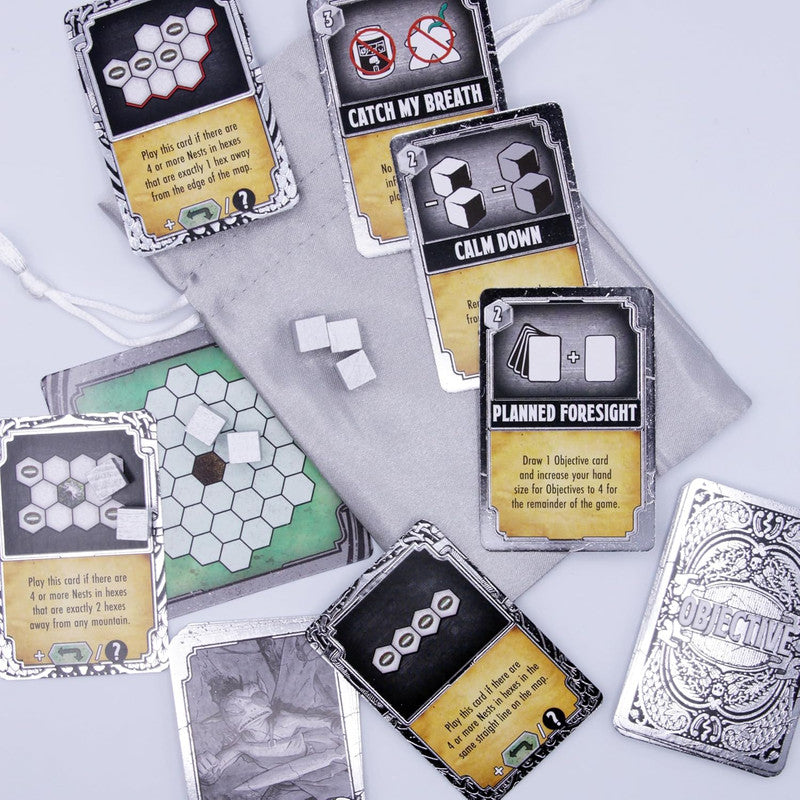Board game components spread out: several cards, white hexagonal tokens, a game board, and a grey bag