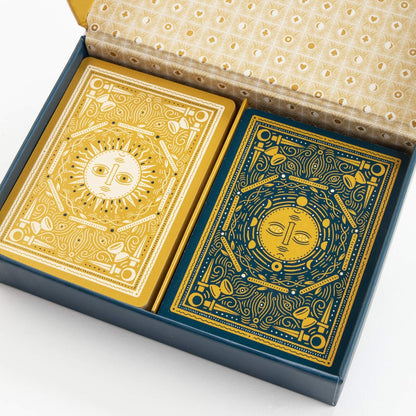 Ornate card game set: gold sun deck and blue celestial deck in an open navy box with patterned lid
