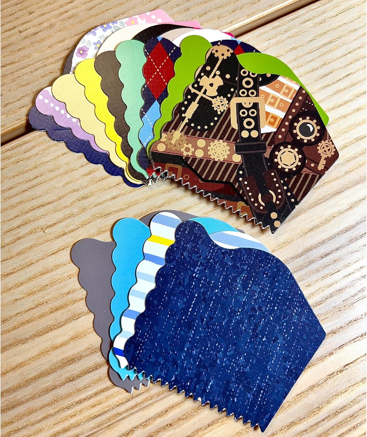 Two fanned stacks of colorful, patterned paper craft samples with decorative edges, including steampunk, argyle, and stripes, on wood