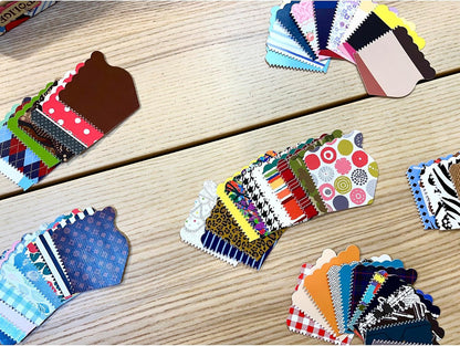 Colorful, cupcake-shaped paper swatches are fanned out in stacks on a wooden table