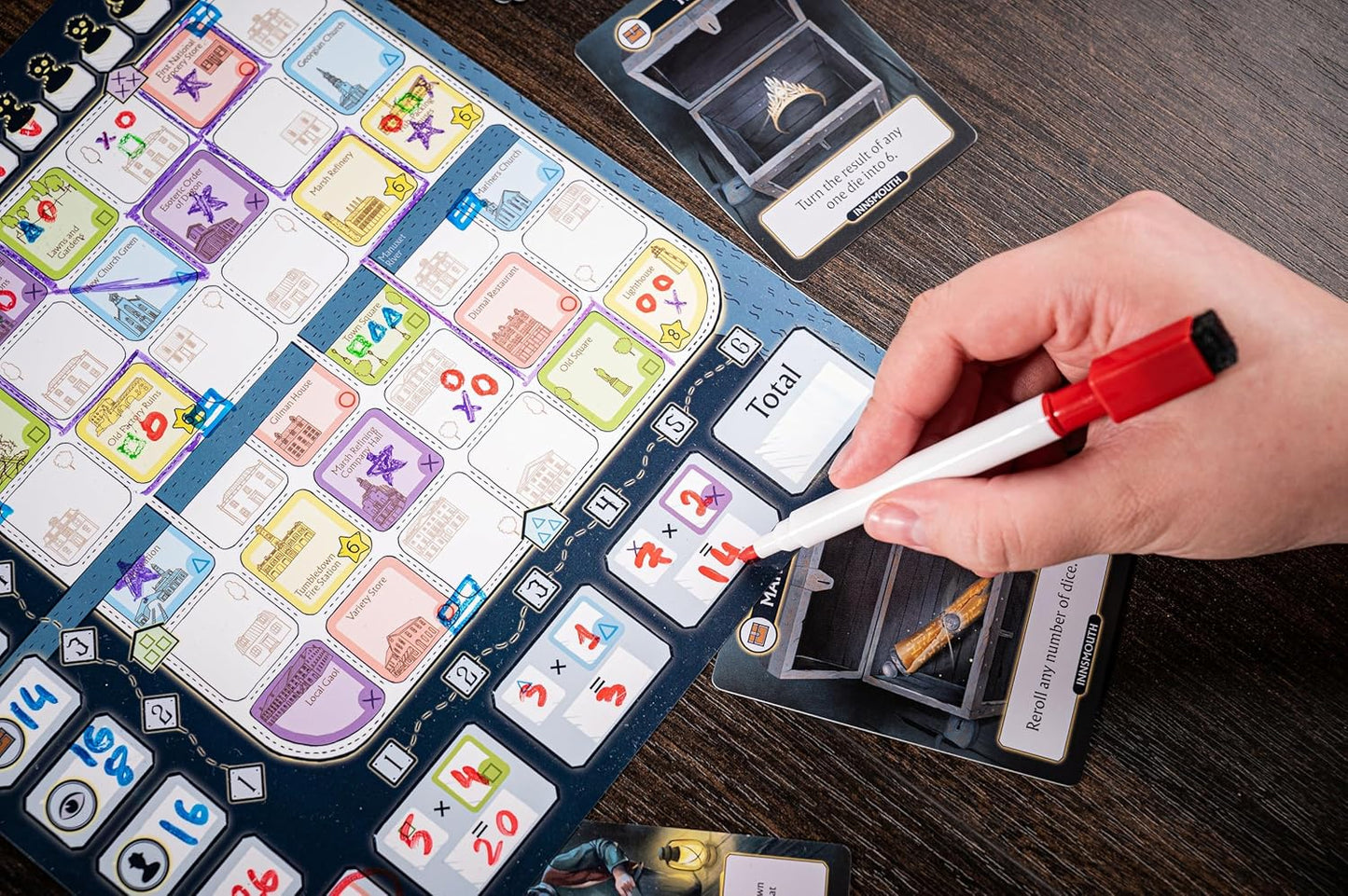 Hand marking scores with a red marker on a colorful, laminated roll-and-write board game