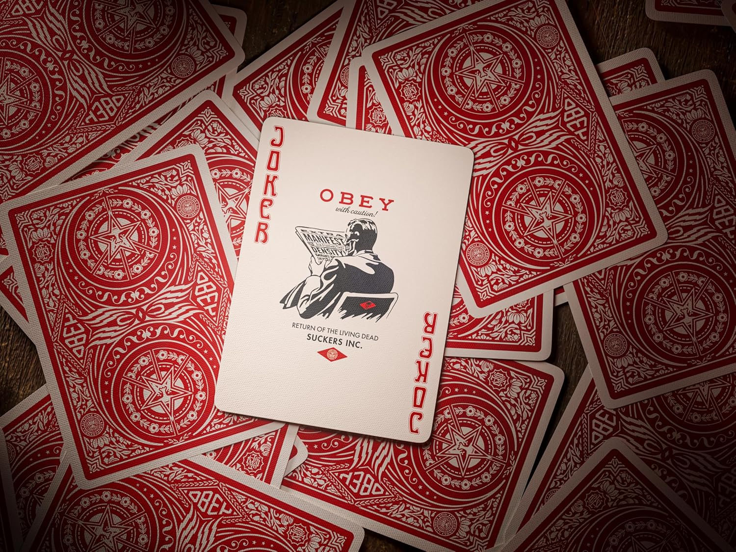 Stylized Joker playing card featuring "OBEY" illustration, surrounded by scattered red-backed cards