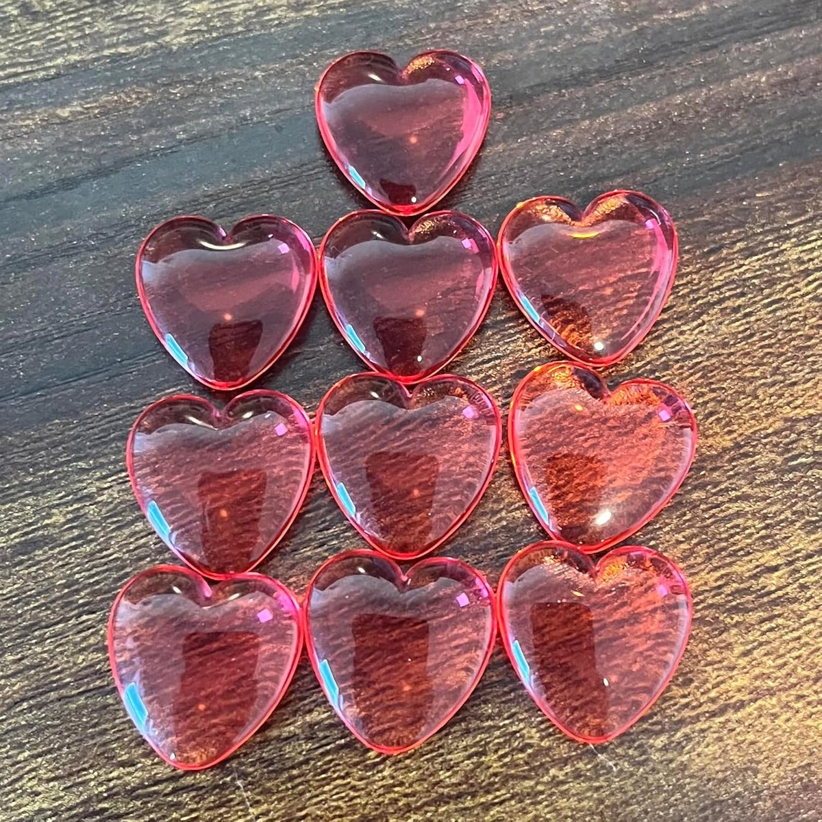 Ten translucent red heart gems are arranged in a pyramid on a dark wood surface.
