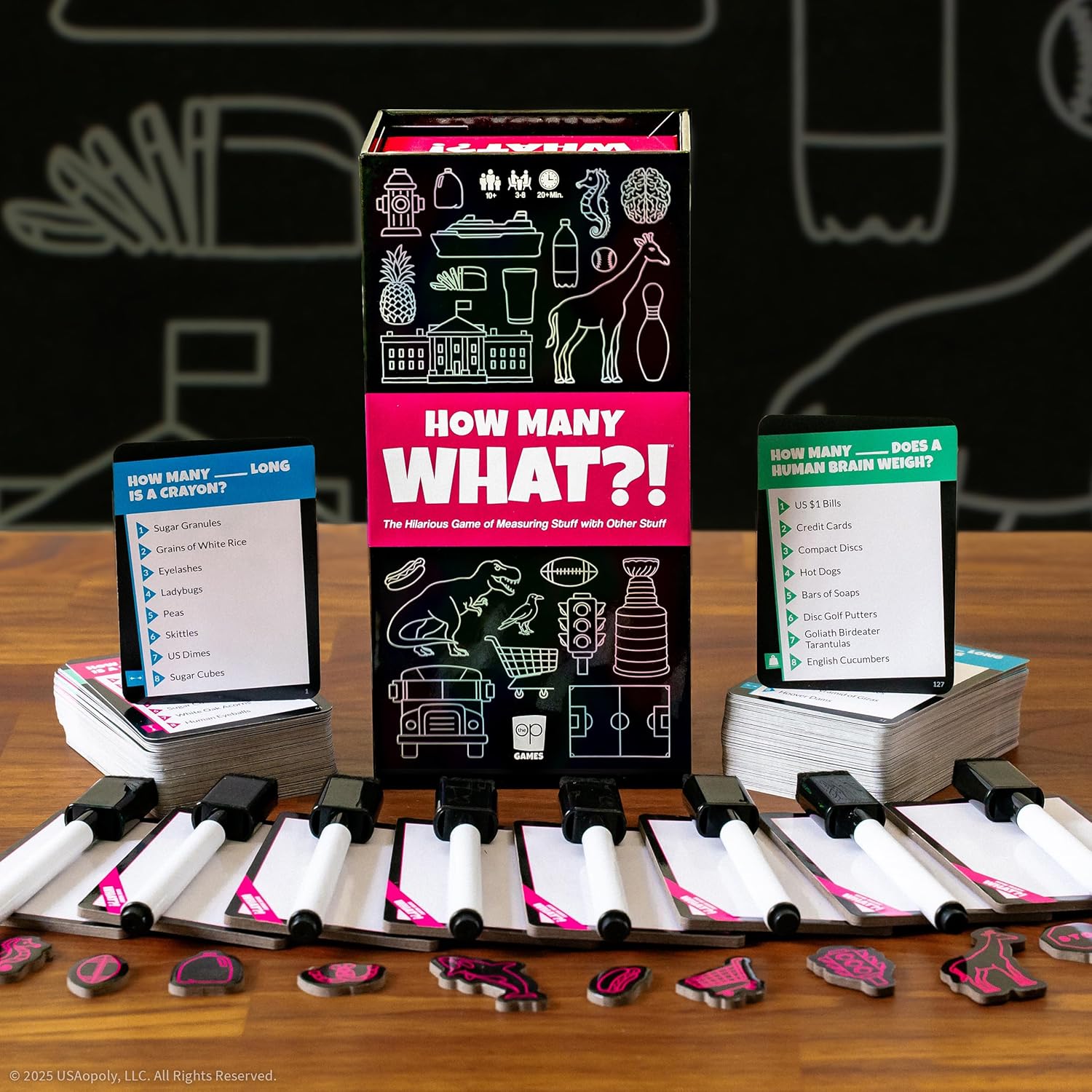 Game components for "How Many WHAT?!" laid out, including the box, question cards, and player dry-erase boards