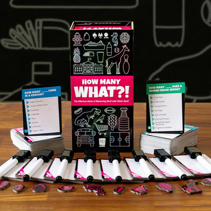 Game components for "How Many WHAT?!" laid out, including the box, question cards, and player dry-erase boards