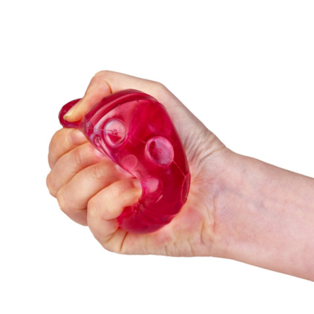 The translucent red Smooshos Super Squeeze Dice is compressed by a hand, revealing its soft gel texture
