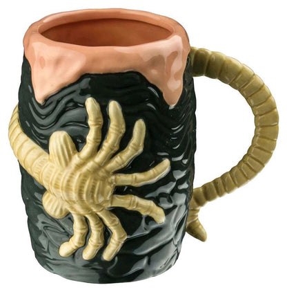Ceramic mug featuring a pale Facehugger creature gripping the black textured body; the tail forms the handle