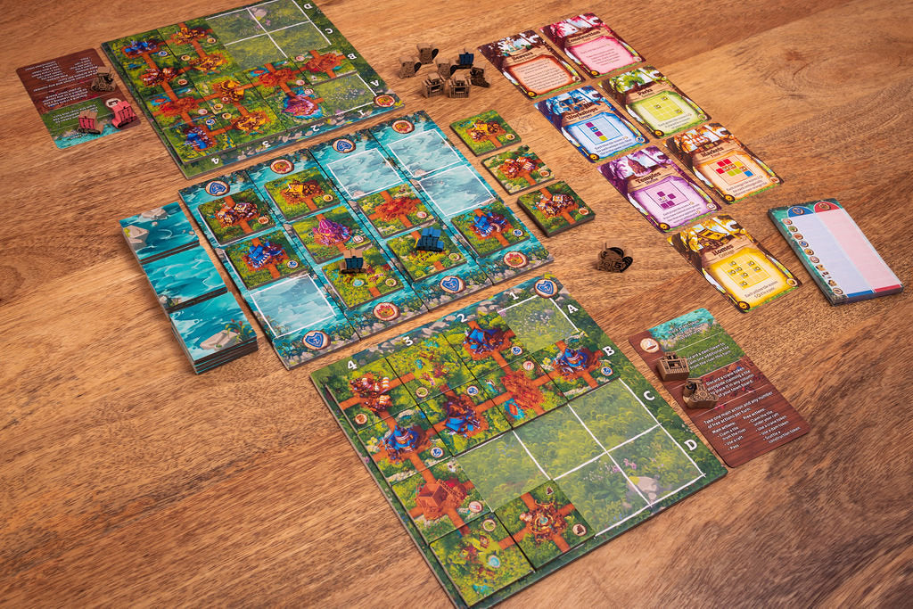 Timber Town board game components spread across a wooden table, including colorful tiled game boards, stacks of cards, and wooden resource tokens