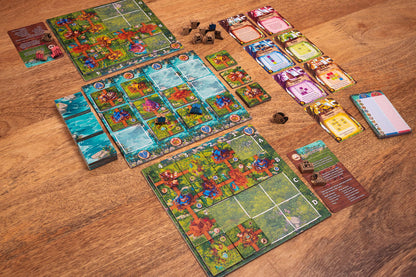 Timber Town board game components spread across a wooden table, including colorful tiled game boards, stacks of cards, and wooden resource tokens