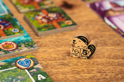 A wooden animal game piece from Timber Town holding a sign with a 5, surrounded by colorful game tiles on a wooden table