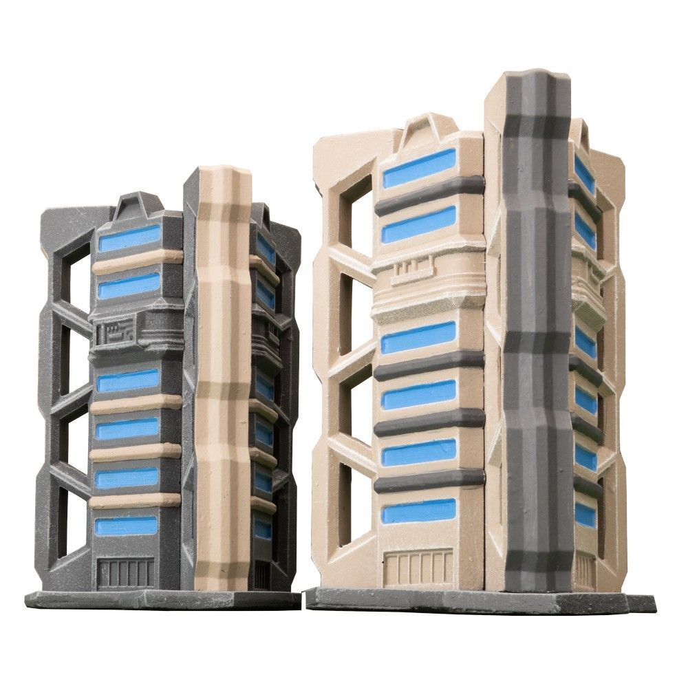 Two miniature Trinity City Tri-Tower terrain pieces, one gray and one tan, with blue window-like details, stand against a white background