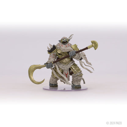A hulking, bandaged creature miniature with gold armor and a horned head, wielding a large staff with a curved golden blade