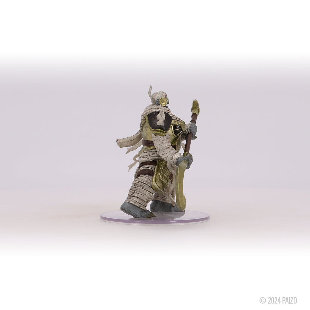 A fantasy miniature of a mummy in gold armor strides forward, holding an ornate staff