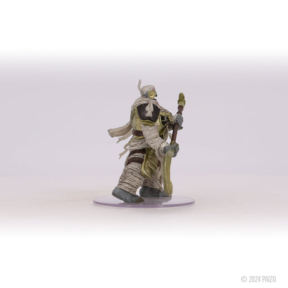 A fantasy miniature of a mummy in gold armor strides forward, holding an ornate staff