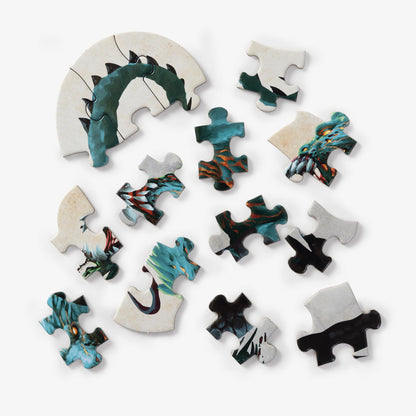 Various pieces of a Clarkson Potter Dungeons & Dragons Mini Shaped Demogorgon Edition jigsaw puzzle, partially assembled and scattered, depicting a green and blue monster with orange accents