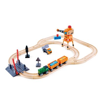 Wooden toy train track set with cargo train, loading crane, dump truck, and crossing accessories