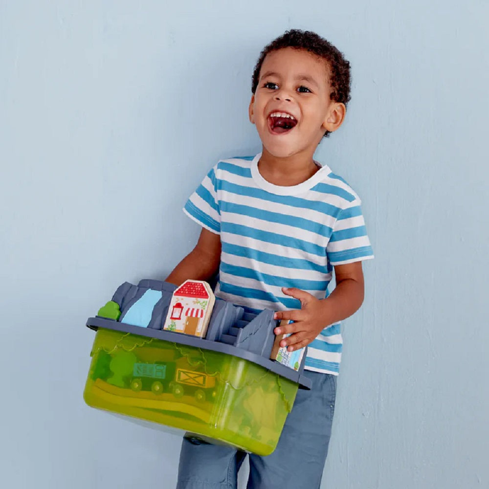 Laughing toddler holding a large green portable toy playset container