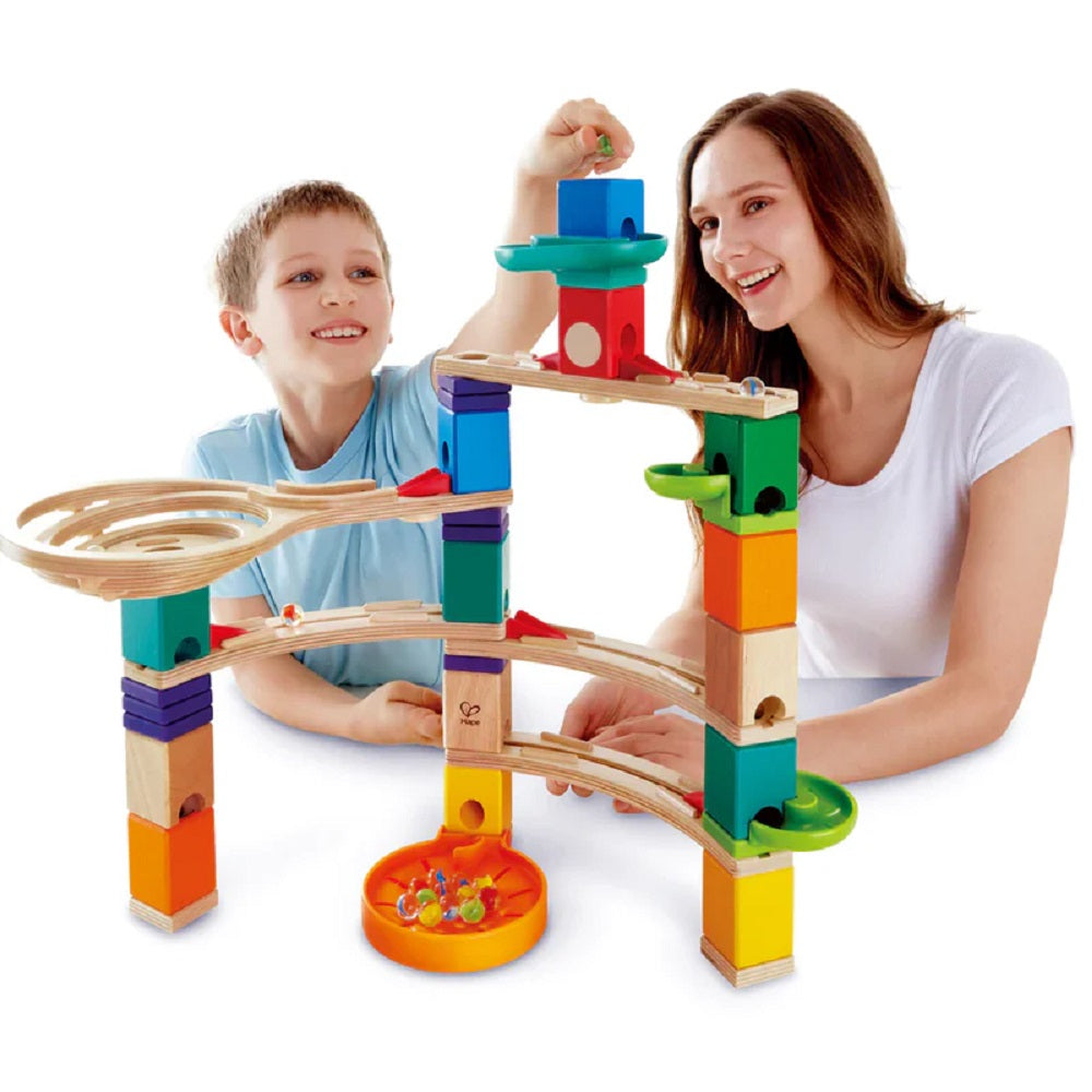 Boy and woman happily use a colorful wooden marble run toy, placing a marble at the start