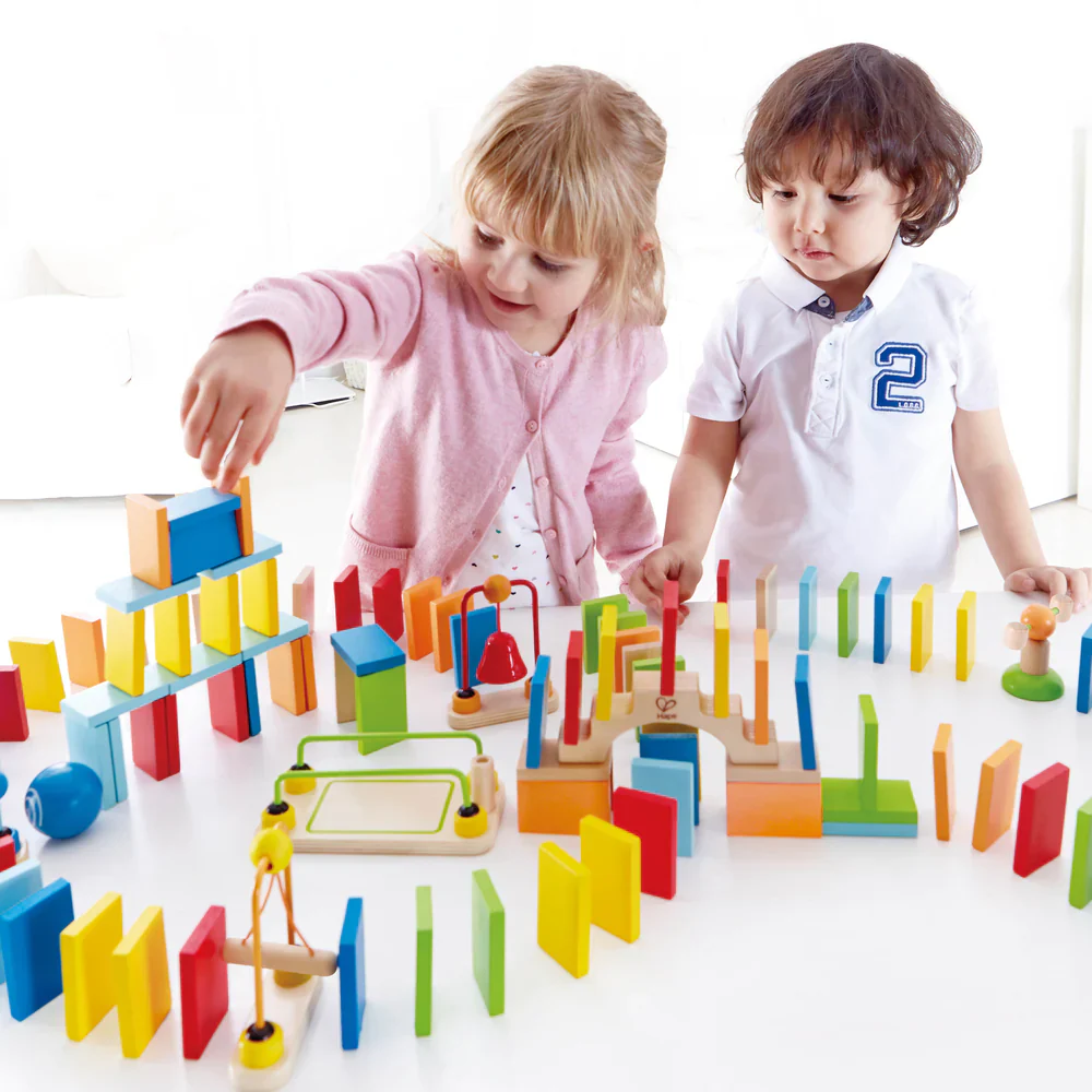 Children intently build a chain reaction structure using colorful wooden dominoes