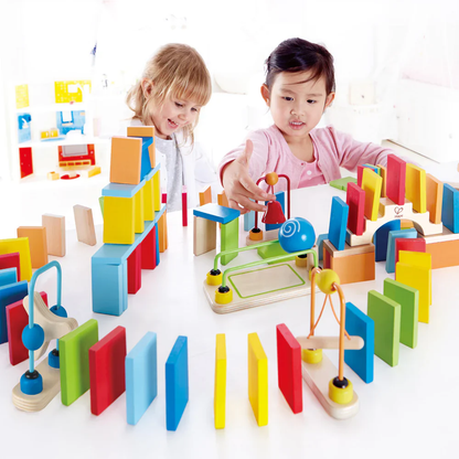 Two girls playing and building an elaborate chain reaction path with colorful wooden dominoes and toys