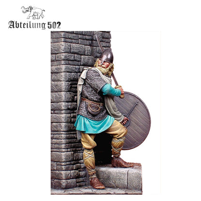 A detailed AK Interactive Historical Resins Viking Warrior 9Th-10Th C Figure 54mm holding a sword and shield stands by a stone wall