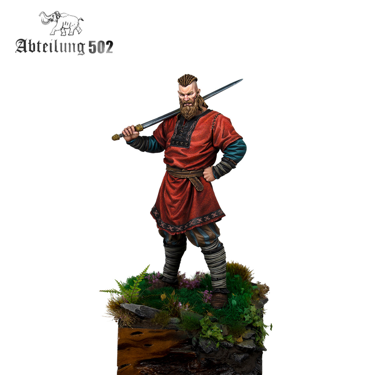 A miniature Ubbe figure with a beard and braided hair in a red tunic holds a sword over his shoulder, standing on a textured base with greenery and rocks