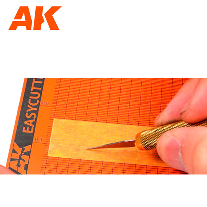 Hand using a precision knife to cut a thin yellow strip on an orange grid cutting mat