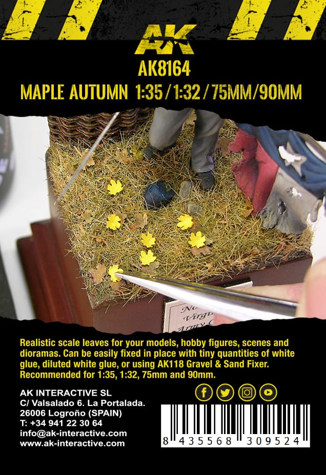 A hand uses tweezers to place a tiny yellow maple leaf onto a grassy diorama base with other autumn foliage