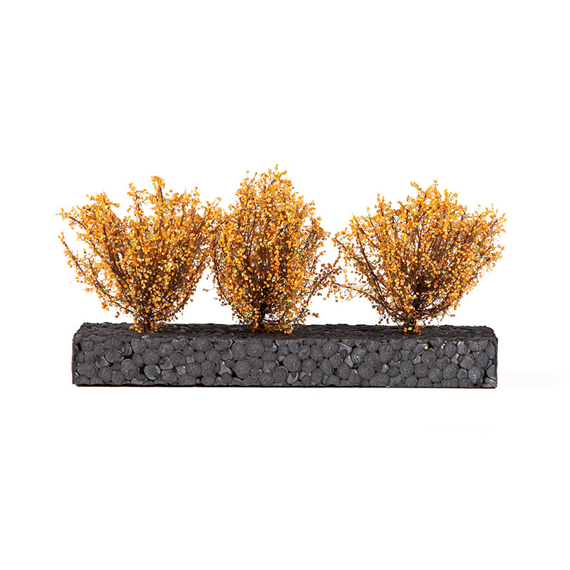 Three golden-orange model shrubs on a dark, pebbled rectangular base