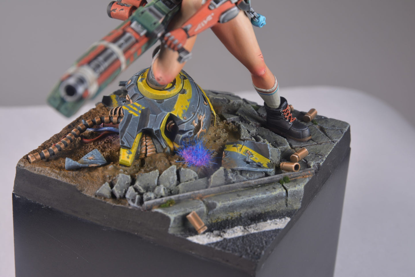 A sci-fi figure stands over a glowing -  broken robot helmet on a rubble-strewn road -  holding a large weapon