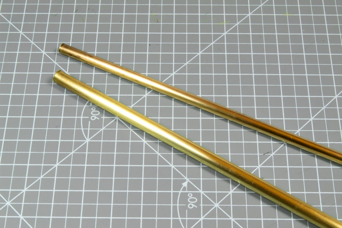 Two parallel brass rods on a grey cutting mat with a measurement grid and 90-degree angle marks.