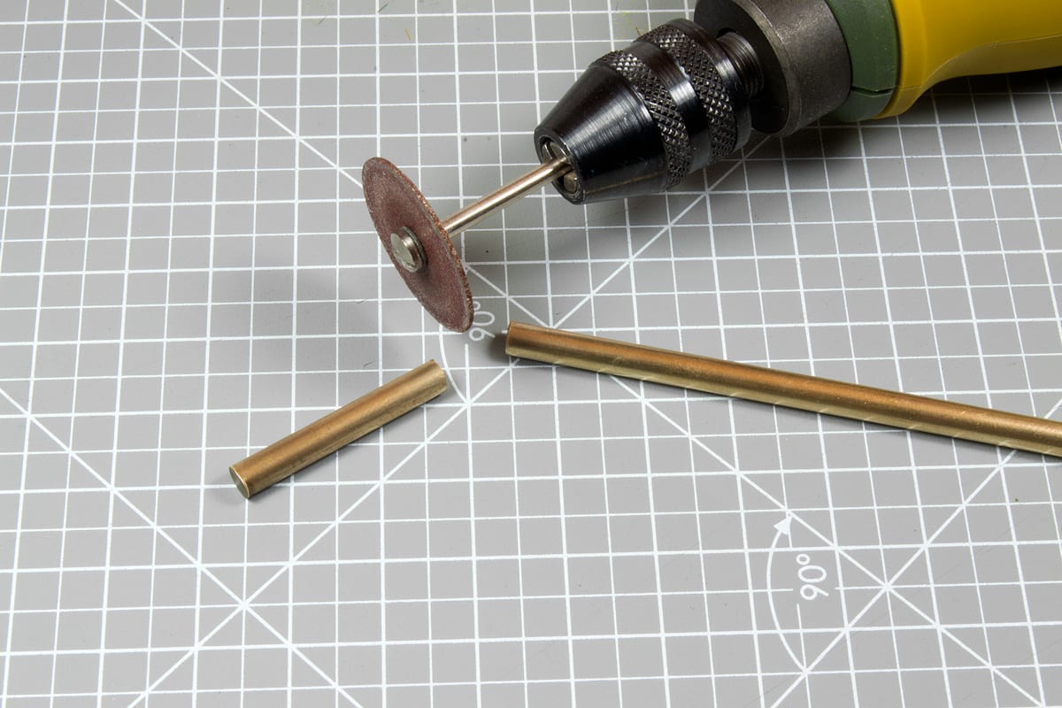 Rotary tool with cutting disc next to a brass rod, freshly cut in half, on a grey grid mat.