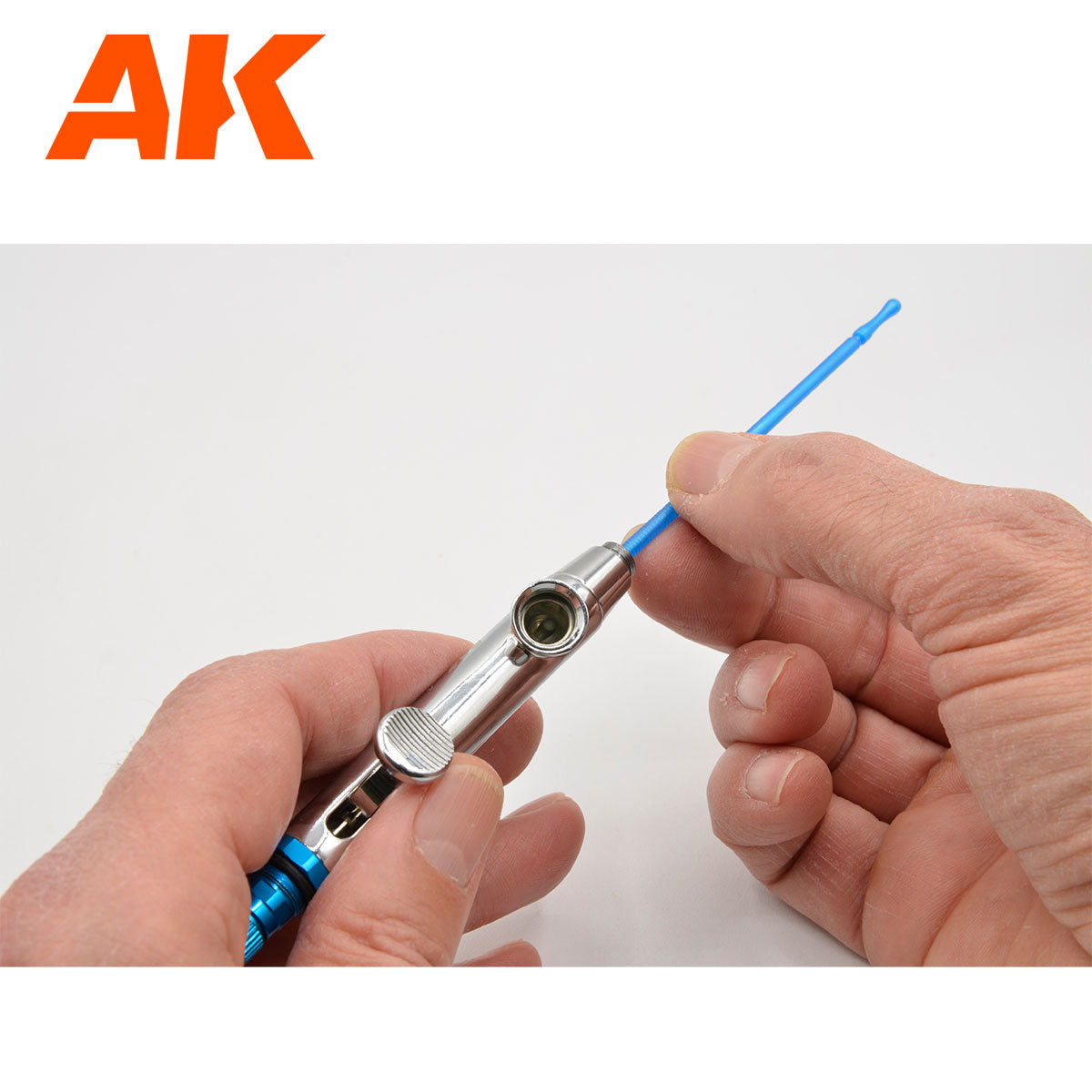 Hands inserting a blue cleaning tool into the paint cup of a silver airbrush