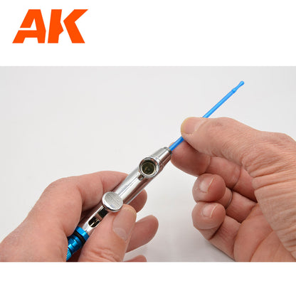 Hands inserting a blue cleaning tool into the paint cup of a silver airbrush