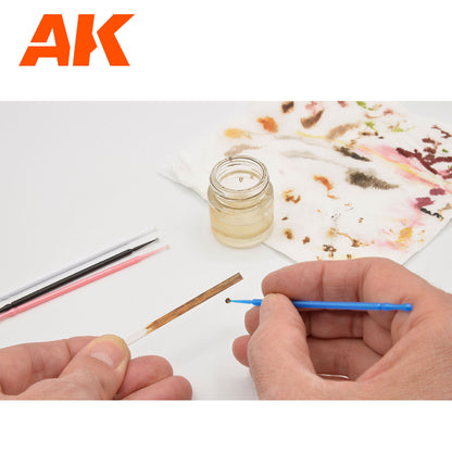 Hands applying a dark liquid to a brown test strip using a blue micro-applicator, a jar of thinner and a stained paper towel are visible