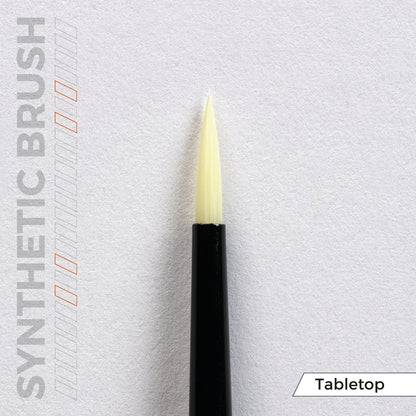 A synthetic brush with a black handle and pointed cream bristles, on a white tabletop background
