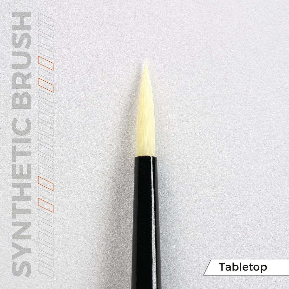 Close-up of a synthetic brush with a black handle and light yellow pointed bristles on a white surface. Text: SYNTHETIC BRUSH