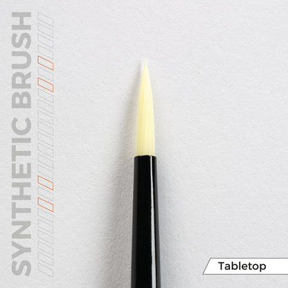 Close-up of a synthetic brush with a black handle and light yellow pointed bristles on a white surface. Text: SYNTHETIC BRUSH