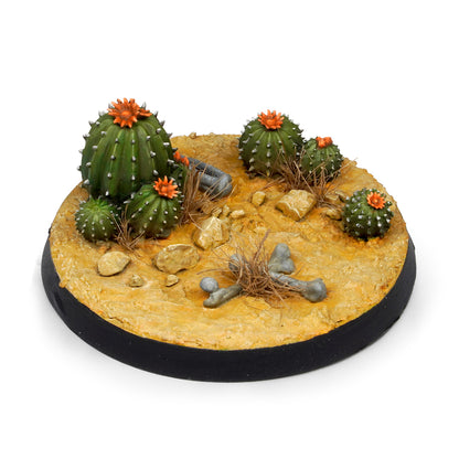 Wargaming desert base with flowering green cacti, dry tufts, scattered rocks, and small bones on arid yellow terrain