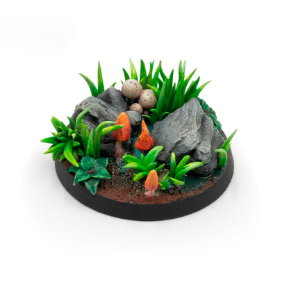 Detailed miniature base featuring rocks, bright green grass, orange fungi, and wet earth
