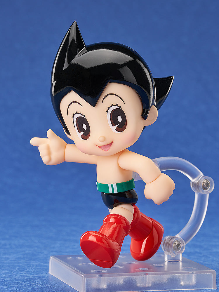 A cheerful Astro Boy figure in red boots and black shorts points forward, standing on a clear display base