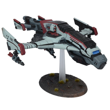 A grey, black and red sci-fi starship miniature with visible weaponry, on a clear stand and textured base.