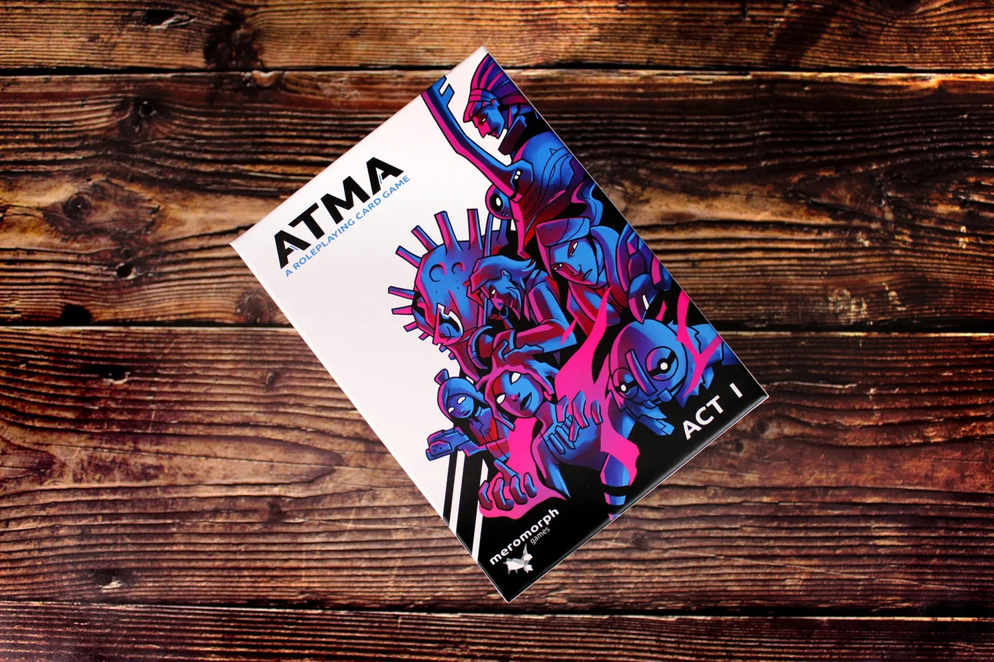 ATMA Roleplaying Card Game box (ACT I) with vibrant blue & pink sci-fi character art, angled on wood