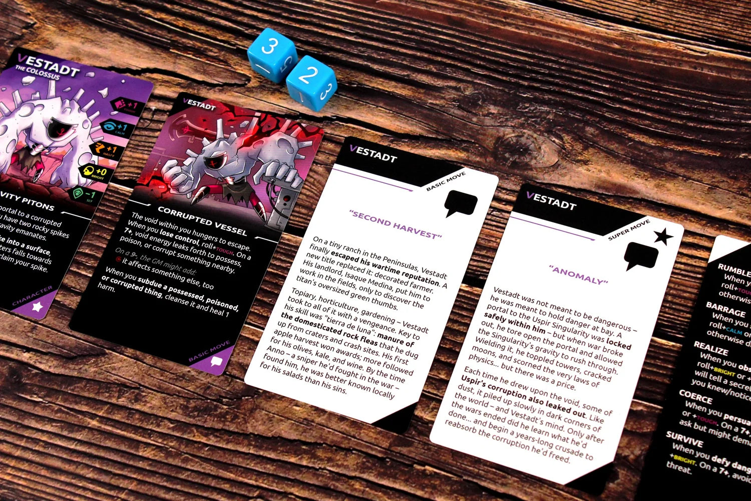 Close-up of board game cards with spiky monster art and text, plus blue dice showing 2 and 3, on a wooden table