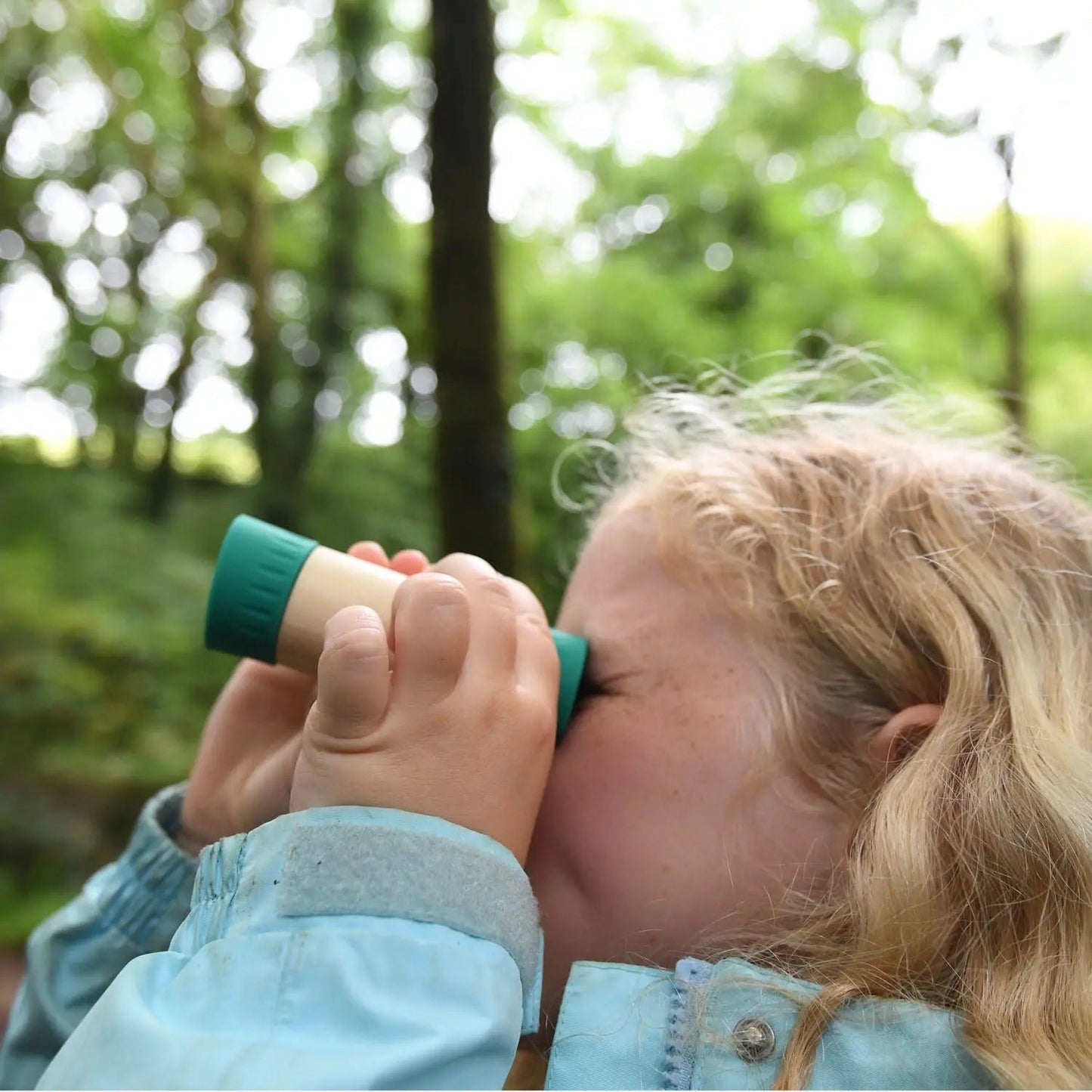 Blonde girl looking through a small monocular in a lush, green forest